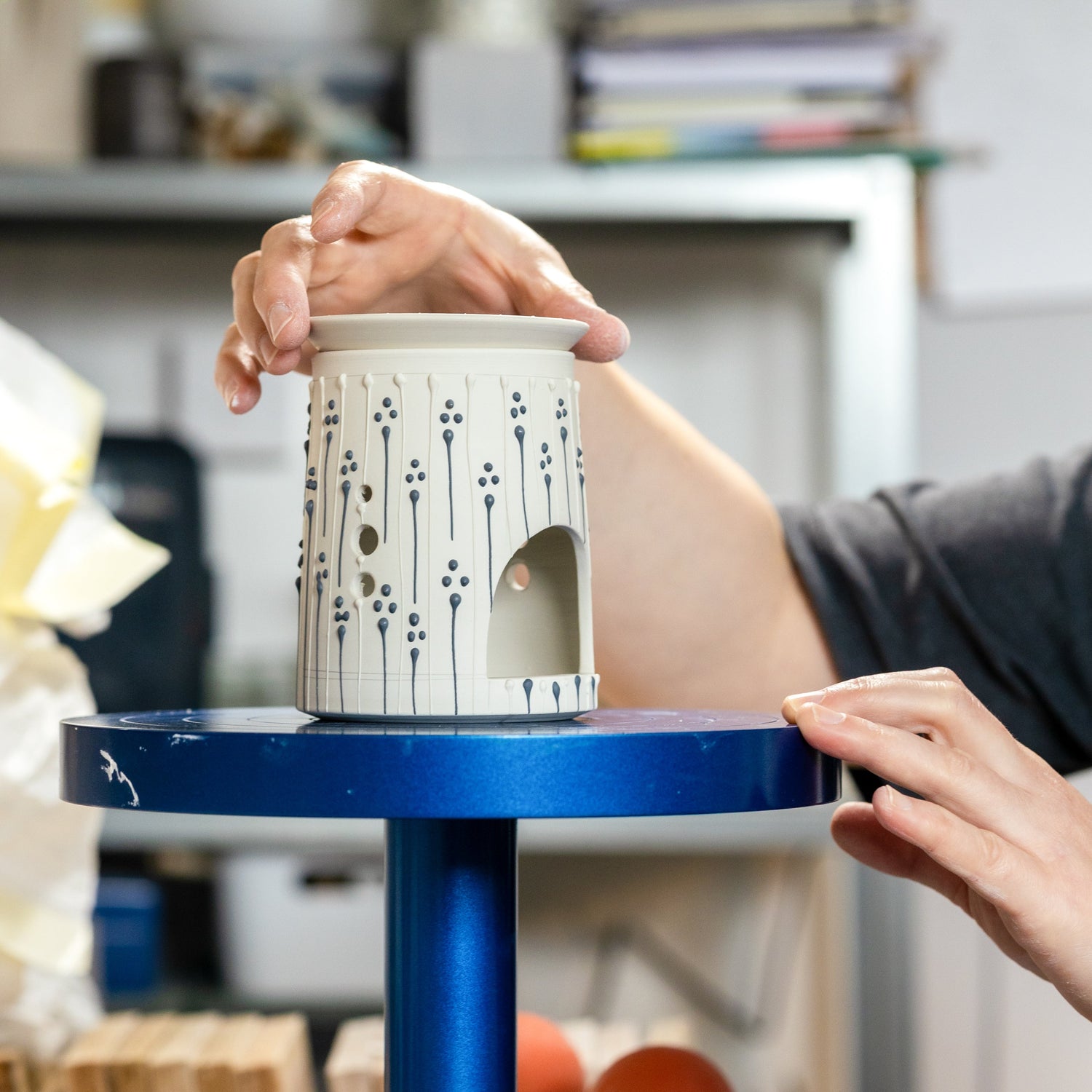 and placing lid on handmade porcelain wax burner with blue slip-trailed decoration in studio