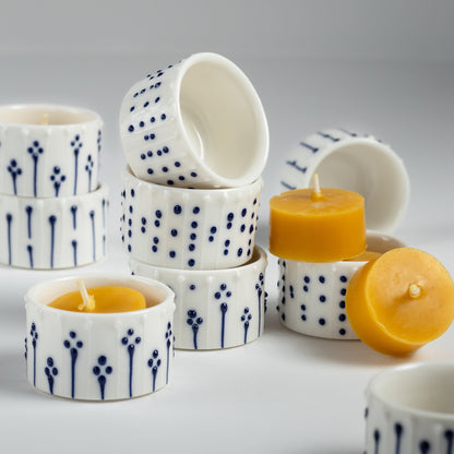 A stack of handmade porcelain tea light holders with various blue and white patterns, shown with natural yellow beeswax tealight candles