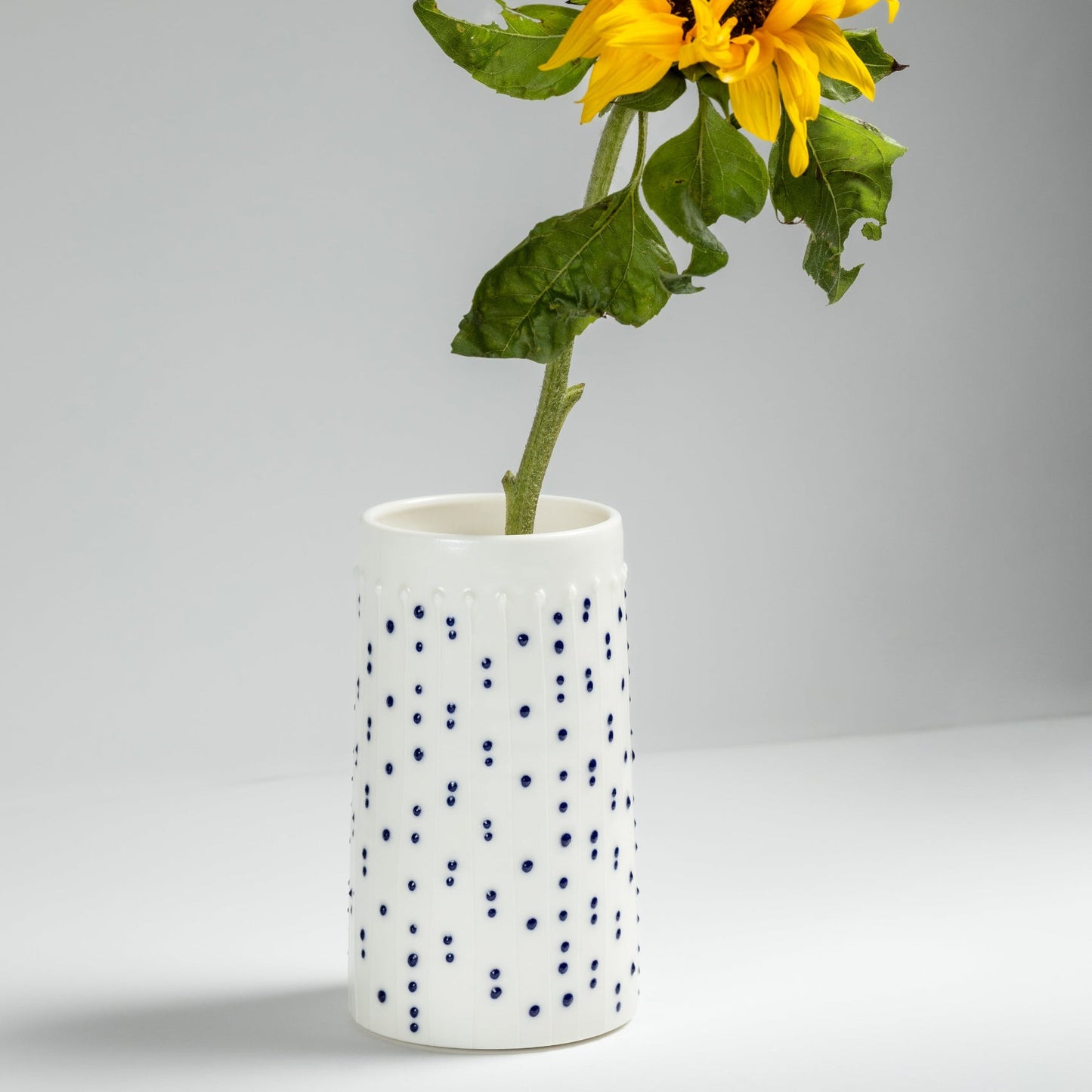 Handmade porcelain tall vases with blue slip-trailed dots and sunflower stem on a gray background