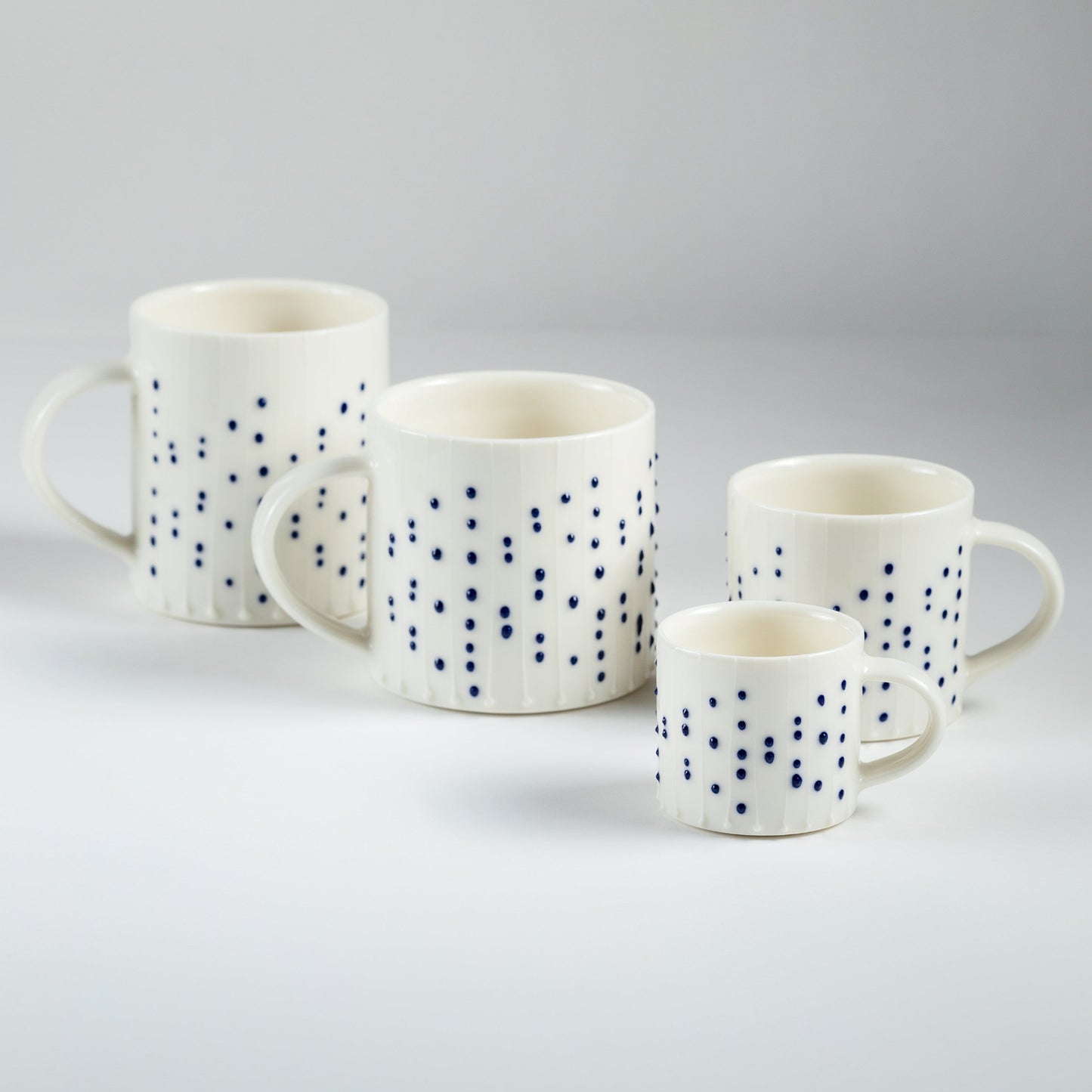 Handmade porcelain mugs in four sizes with blue slip-trailed dot decoration