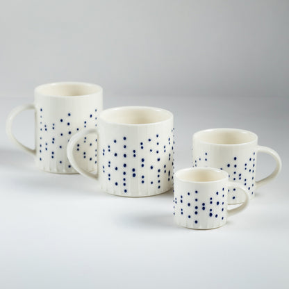 Handmade porcelain espresso cup with blue slip-trailed dot decoration shown beside larger porcelain mugs and cups for size comparison