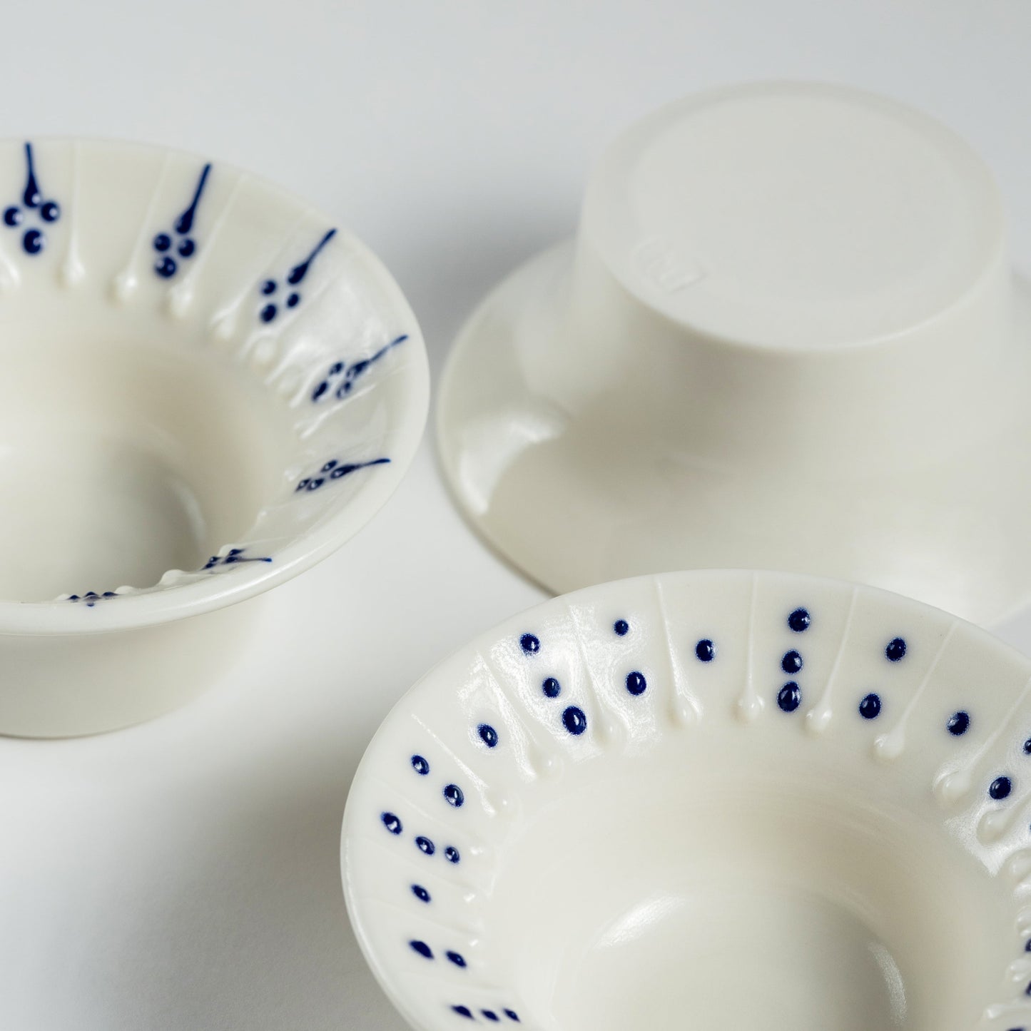 Three handmade porcelain flanged tea light holders with blue slip-trailed decoration, close-up