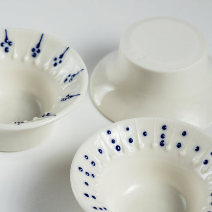 Three handmade porcelain flanged tea light holders with blue slip-trailed decoration, close-up