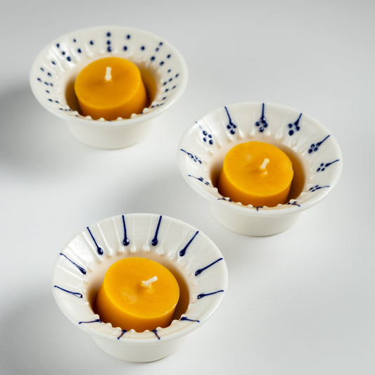 Three handmade porcelain flanged tea light holders with blue slip-trailed decoration, each holding a natural Irish beeswax tealight