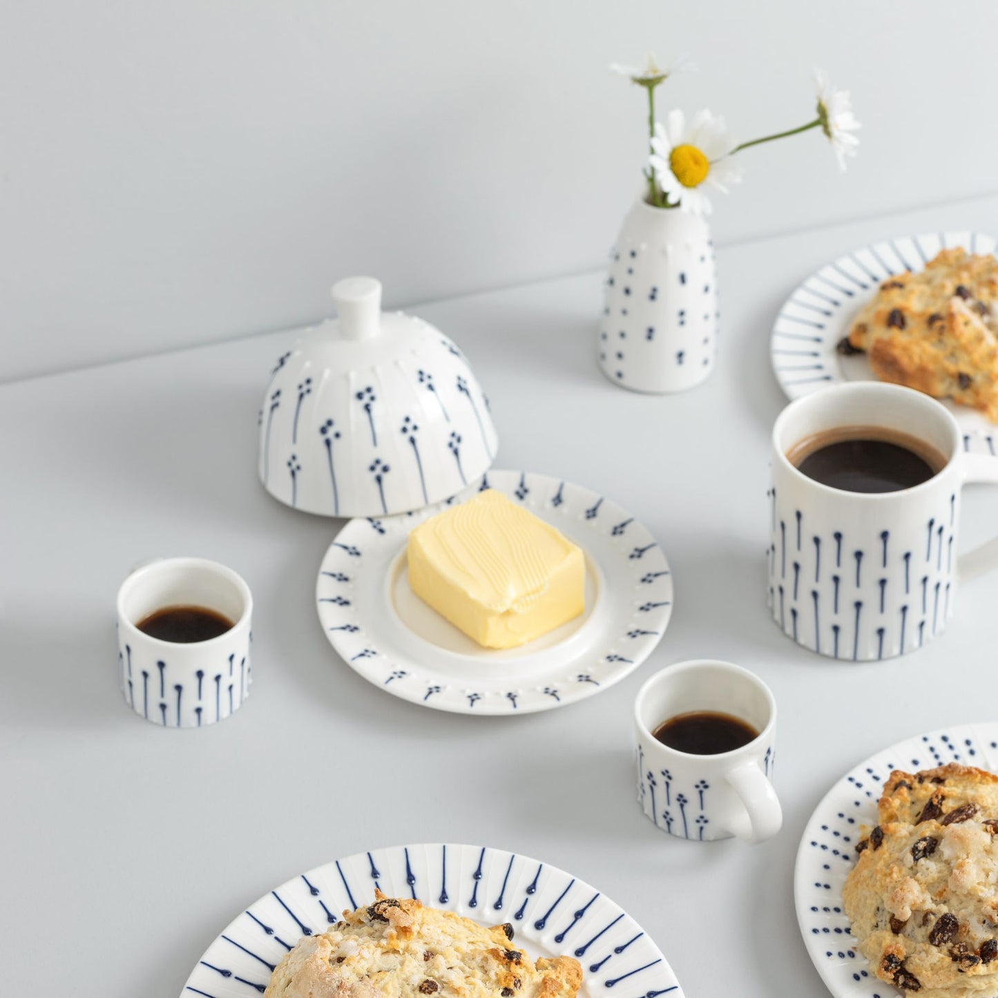 Handmade porcelain breakfast set featuring a blue and white butter dish, espresso cups, and side plates with fresh scones and coffee