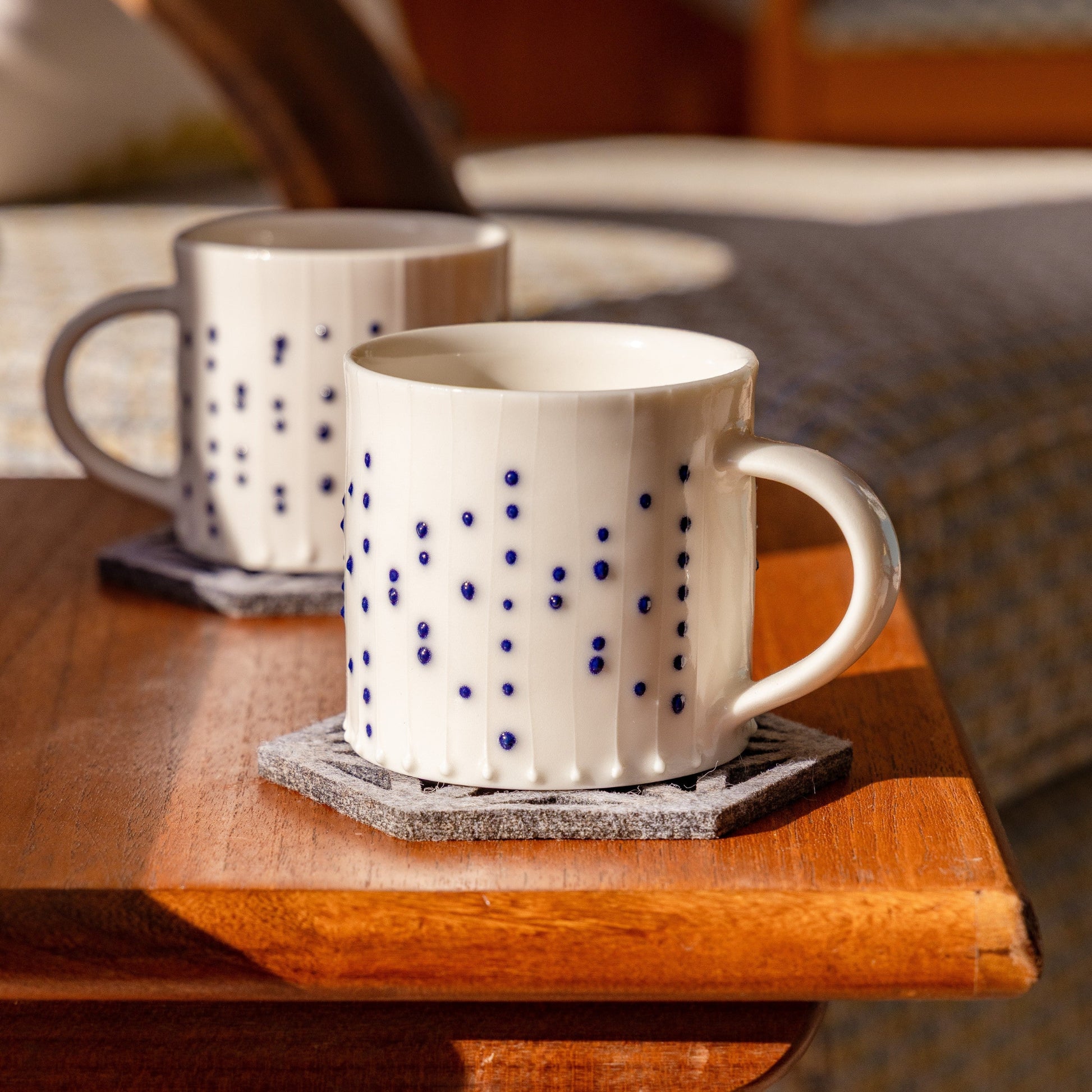 Handmade porcelain small coffee mugs with blue slip-trailed dot decoration on wooden table
