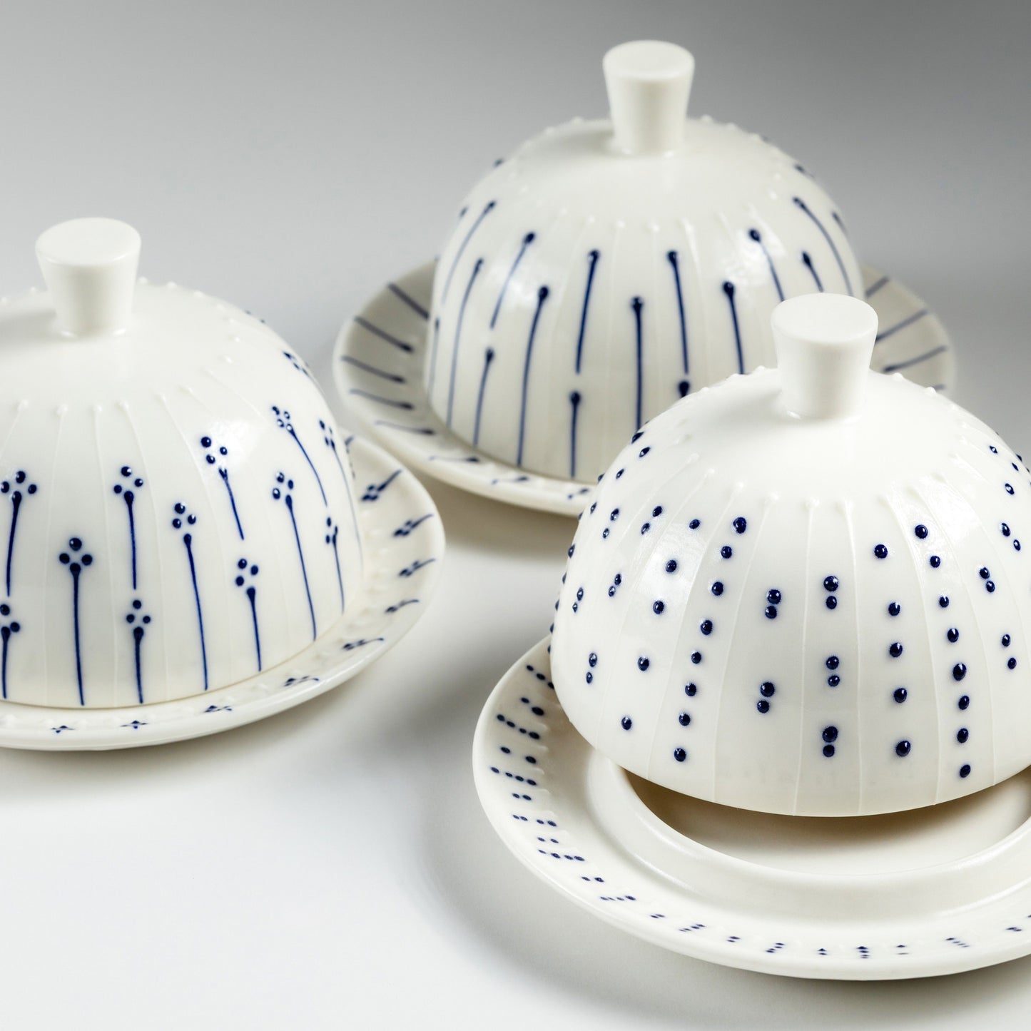 Handmade porcelain butter dishes with blue slip-trailed dot, line, and flower decorations on a grey background