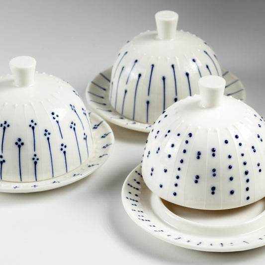 Handmade porcelain butter dishes with blue slip-trailed dot, line, and flower decorations on a grey background