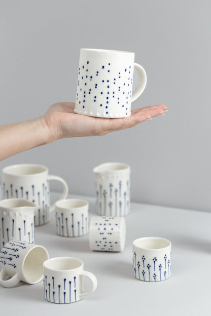 Handmade porcelain tea mug with blue slip-trailed dot decoration held in hand