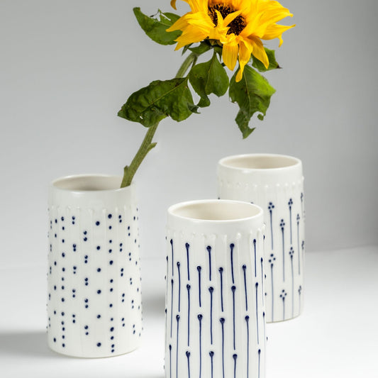 Handmade porcelain tall vases with blue slip-trailed dot and line decoration, one holding a sunflower on a gray background 