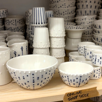 Handmade porcelain bowls and mini bowls with blue slip-trailed decoration displayed on a studio shelf