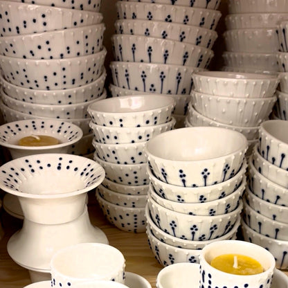 Stacks of handmade porcelain mini bowls with blue slip-trailed decoration displayed on a pottery studio shelf.