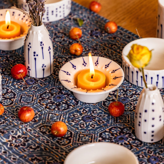 Flanged porcelain tea light holders with beeswax candles styled on a table with handmade porcelain tableware and mini vases