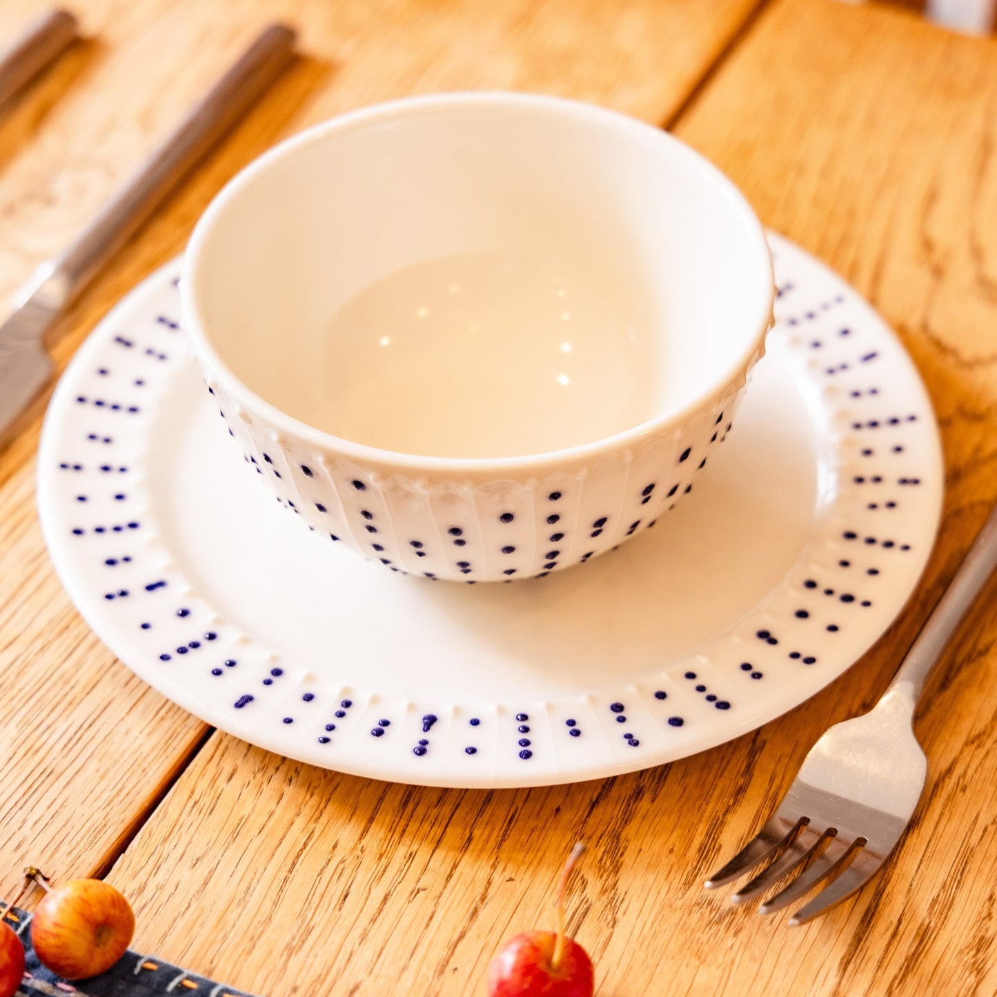 Handmade porcelain breakfast bowl with blue slip-trailed dot decoration on a matching porcelain side plate on a wooden table
