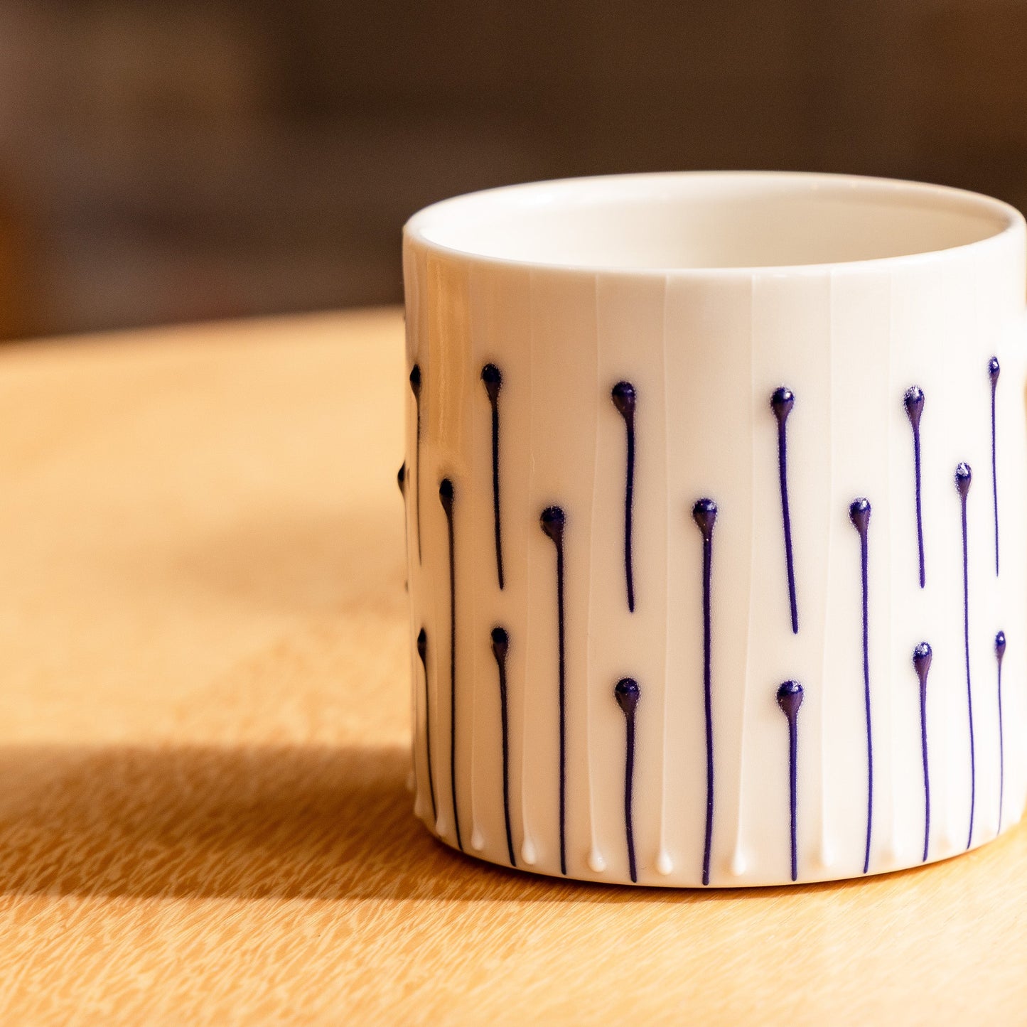 Handmade porcelain tumbler in slip-trailed line pattern on a wooden table