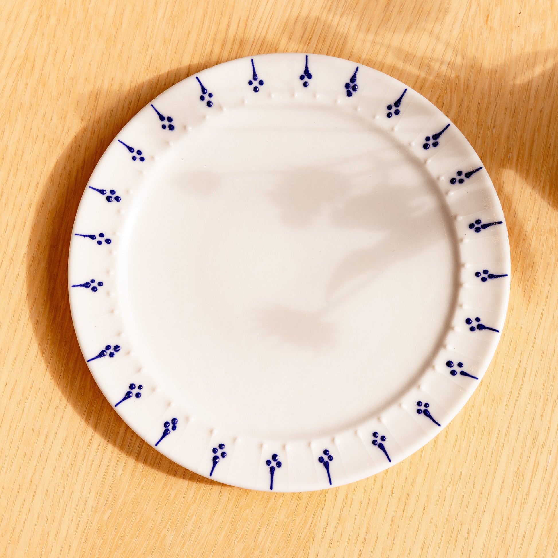 Handmade porcelain side plate with blue flower motif pattern on a wooden table