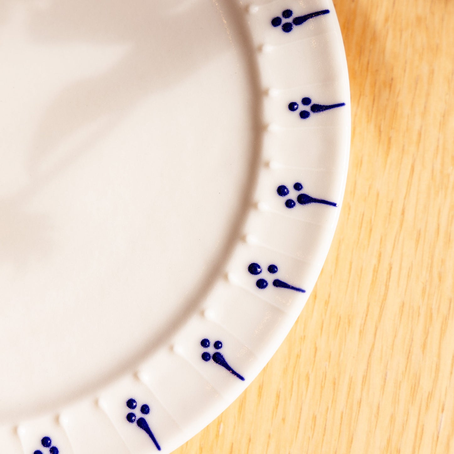 Close-up of handmade porcelain side plate with blue slip-trailed floral decoration on wooden table