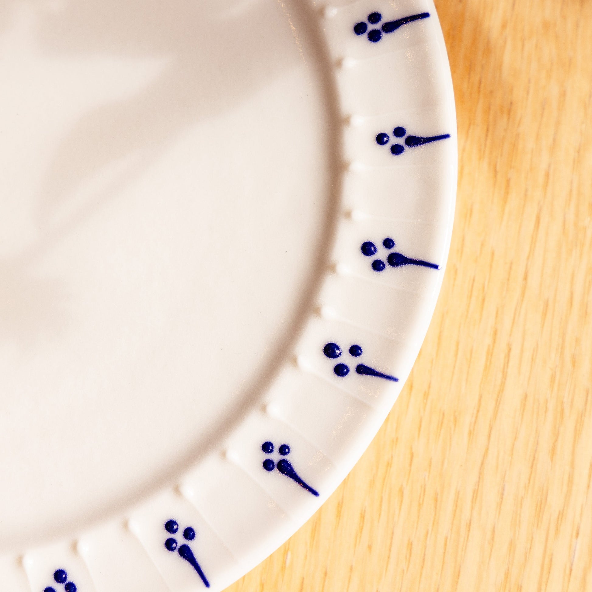 Close-up of handmade porcelain side plate with blue slip-trailed floral decoration on wooden table