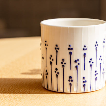 Handmade porcelain tumbler in slip-trailed flower pattern on a wooden table