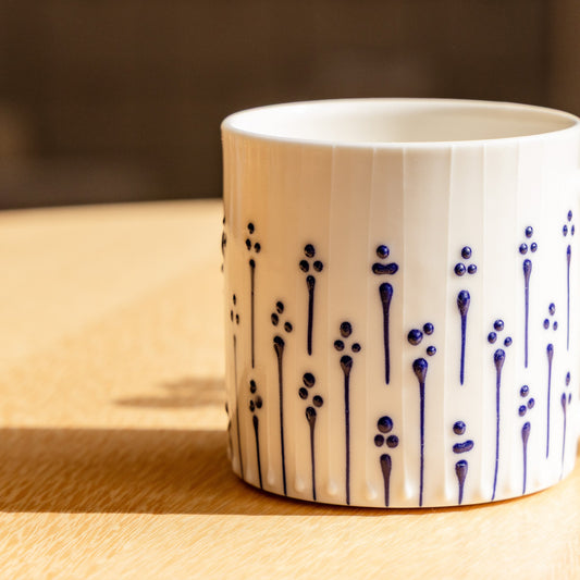 Handmade porcelain tumbler in slip-trailed flower pattern on a wooden table