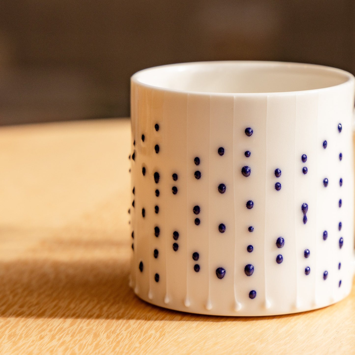 Handmade porcelain tumbler in slip-trailed dotted pattern on a wooden table