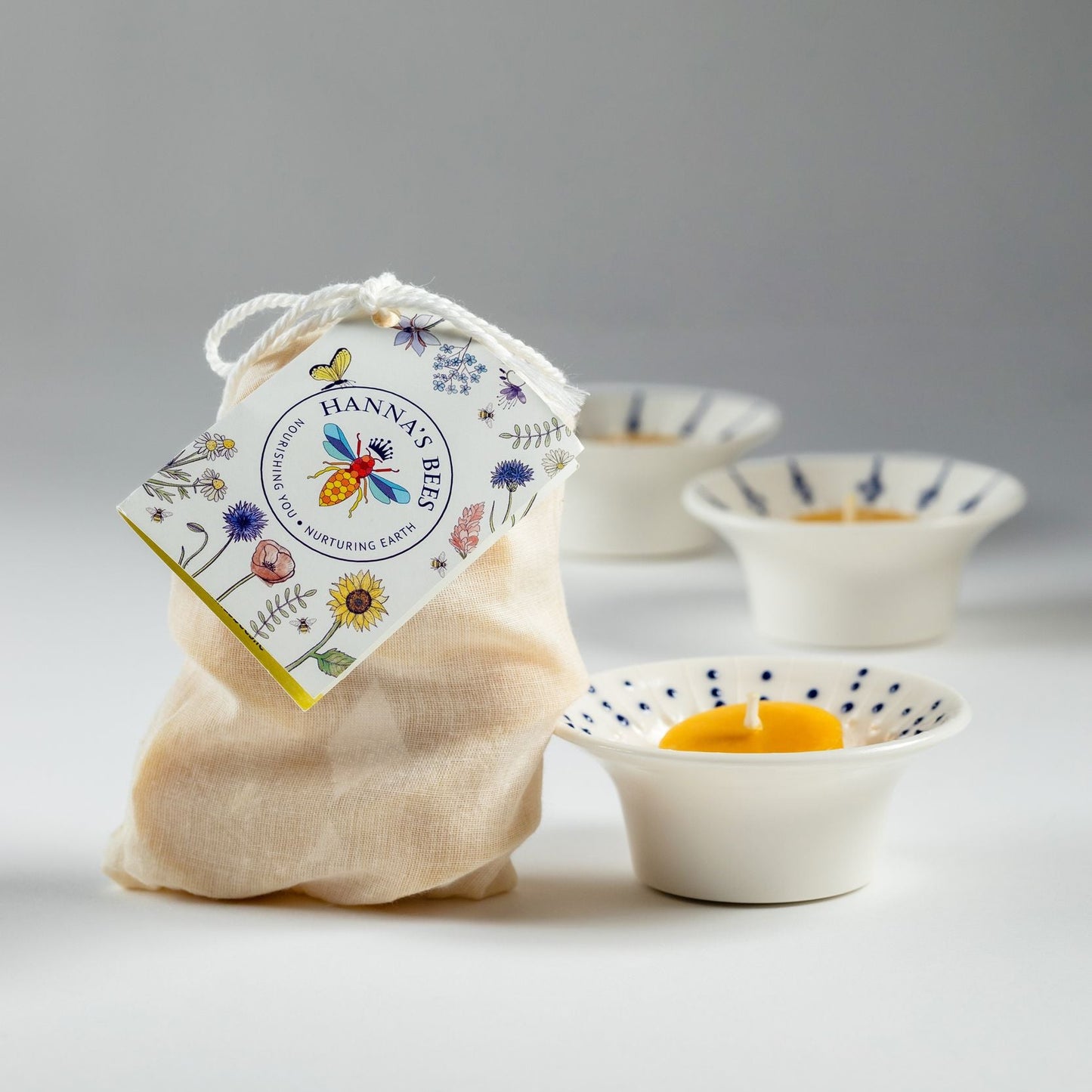 Natural beeswax tealight refills in a cotton bag beside porcelain tealight holders