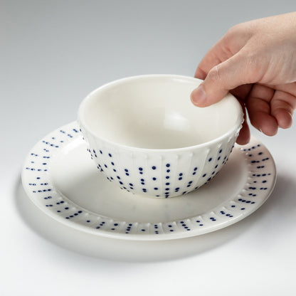 Hand holding handmade porcelain breakfast bowl with blue slip-trailed dot decoration on a matching porcelain side plate