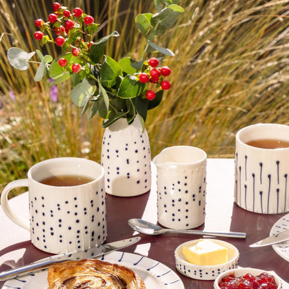 Handmade porcelain milk pourer with blue slip-trailed dot decoration on a breakfast table.