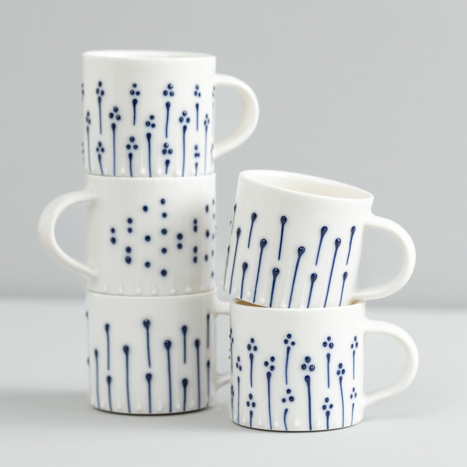 Handmade porcelain mugs with blue slip-trailed dot, line, and flower patterns stacked together