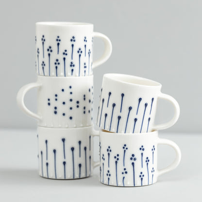Handmade porcelain mugs with blue slip-trailed dot, line, and flower patterns stacked together