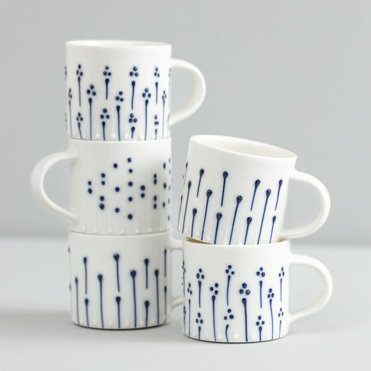Handmade porcelain mugs with blue slip-trailed dot, line, and flower patterns stacked together