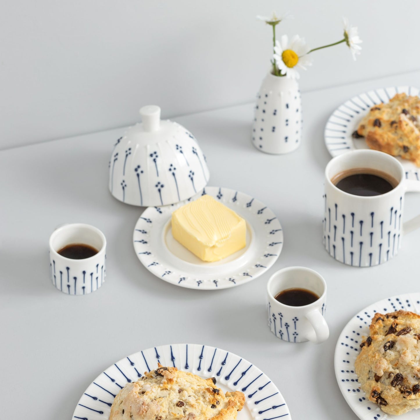 Handmade porcelain espresso cups with blue slip-trailed decoration styled on a breakfast table with mugs, butter dish and plates