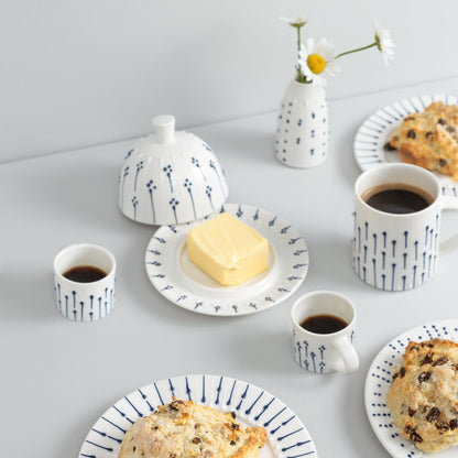 Handmade porcelain espresso cups with blue slip-trailed decoration styled on a breakfast table with mugs, butter dish and plates