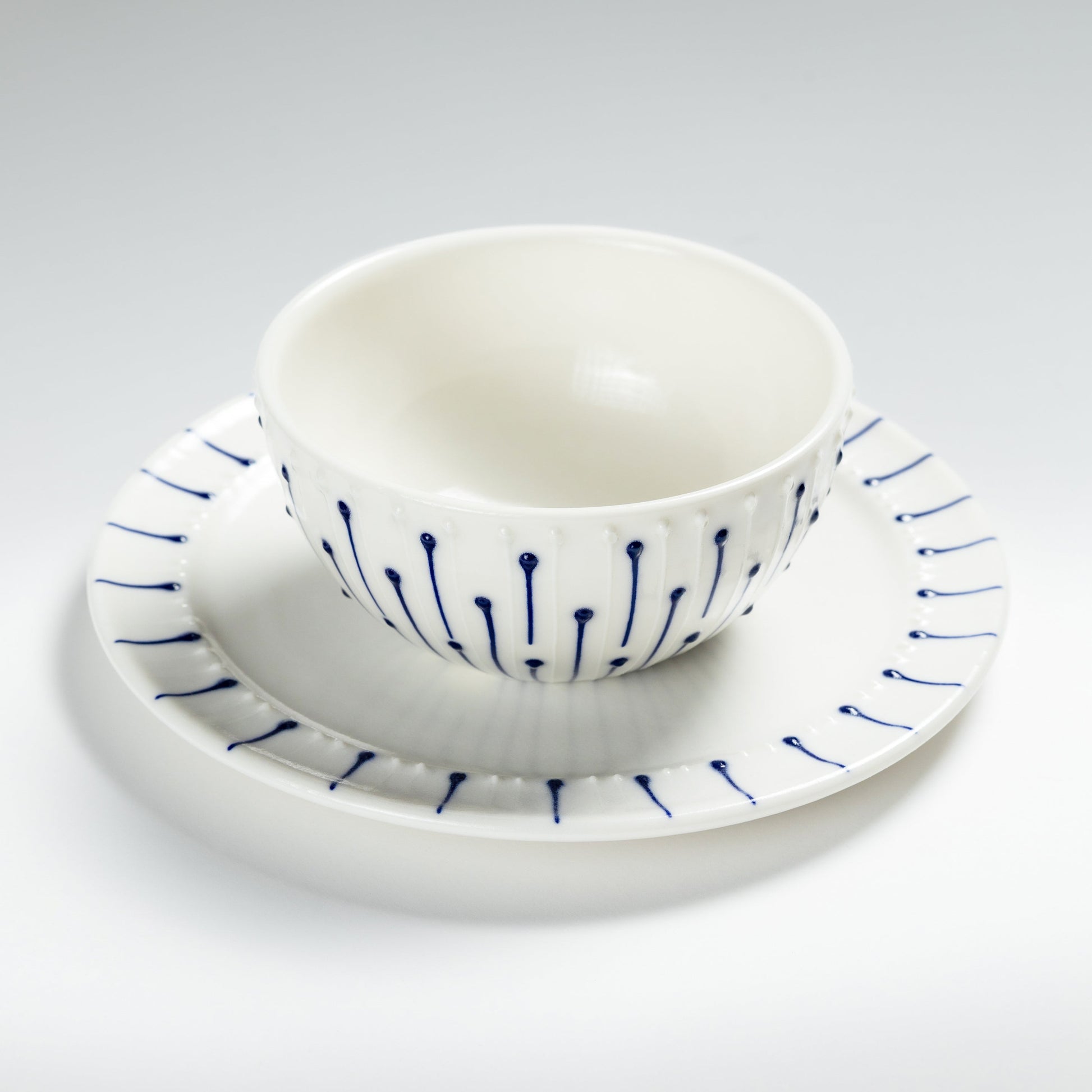 Handmade porcelain breakfast bowl with blue slip-trailed line decoration on a matching porcelain side plate