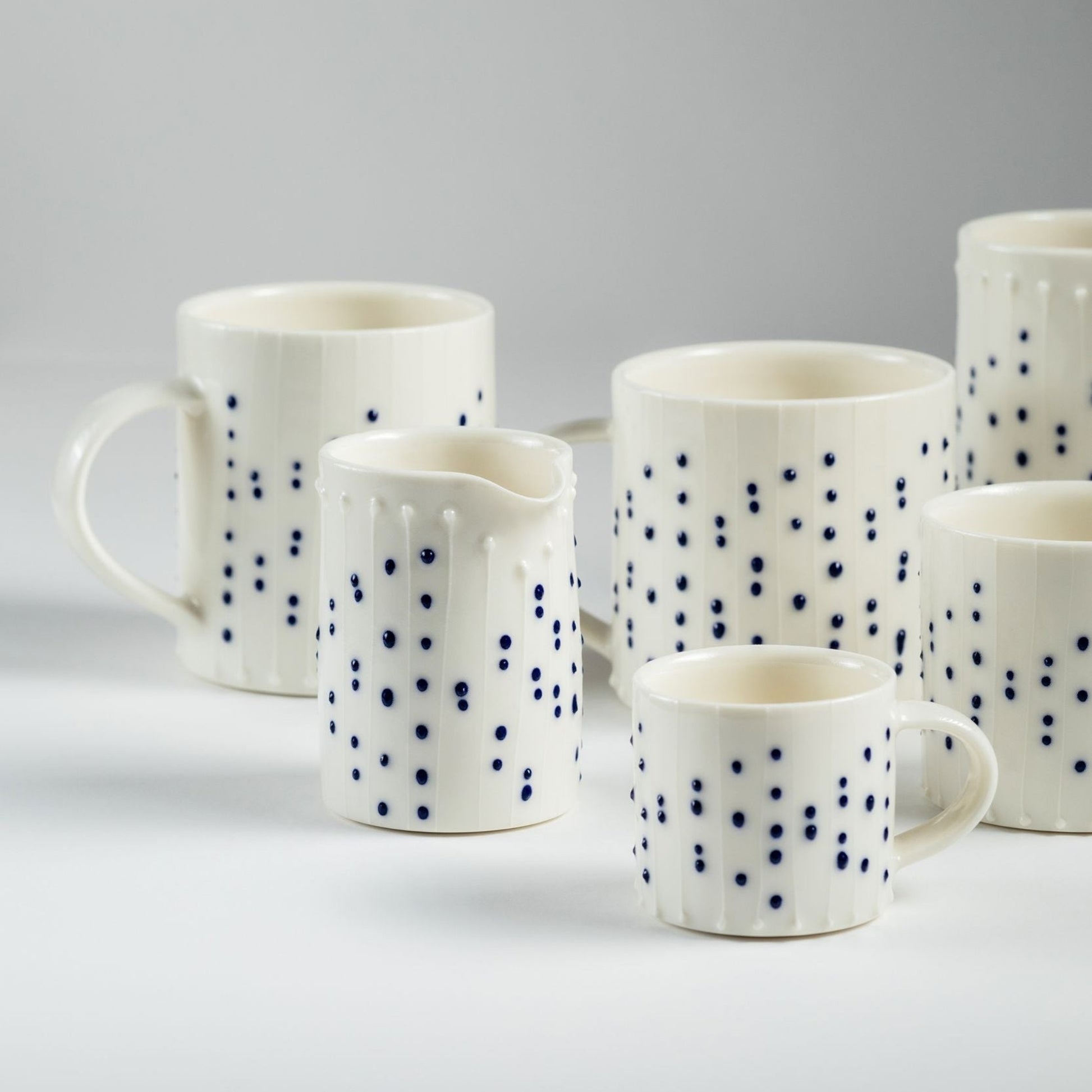 Handmade porcelain mugs and a small milk pourer with blue slip-trailed dot decoration