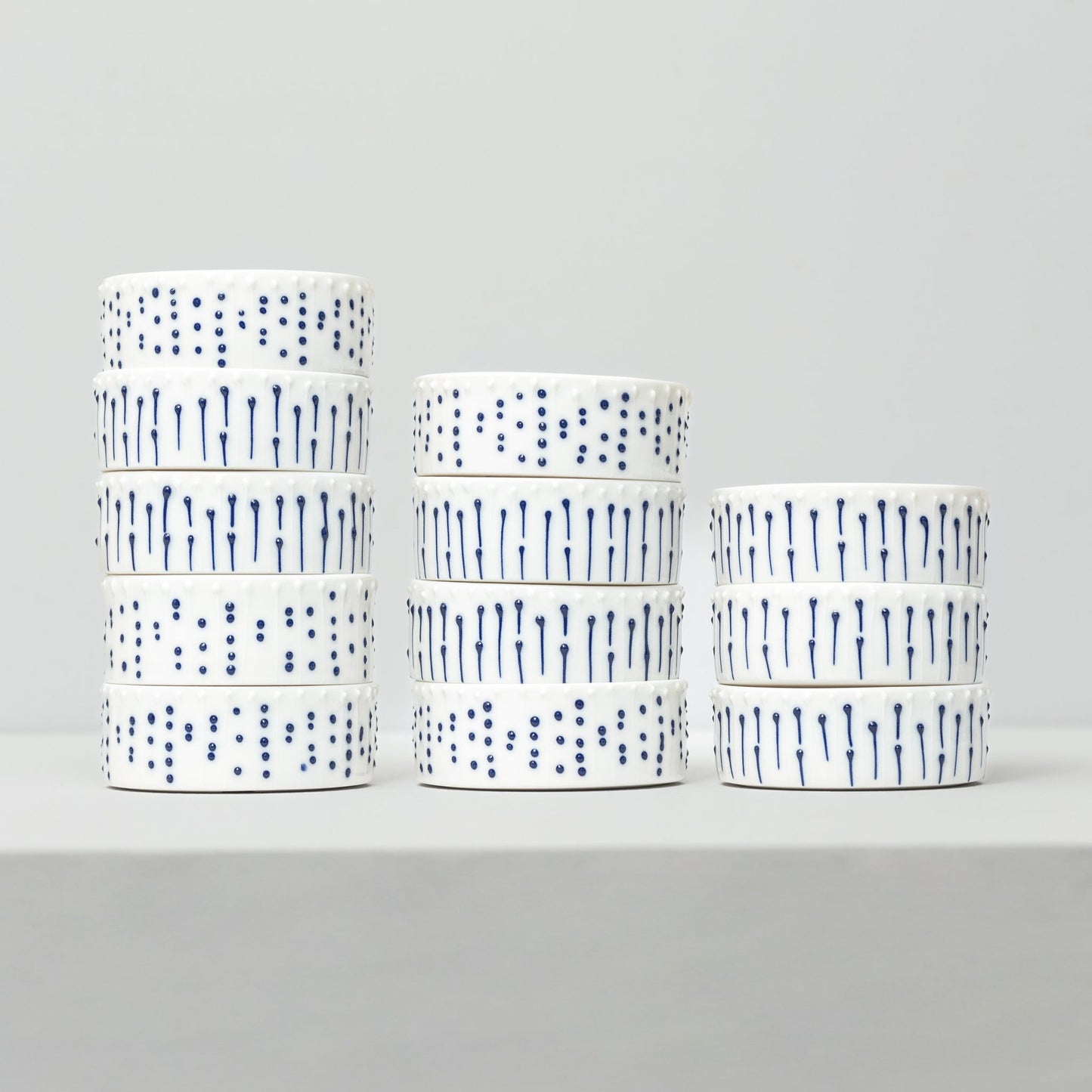 Stacked handmade porcelain ramekins with blue slip-trailed dot and line decoration