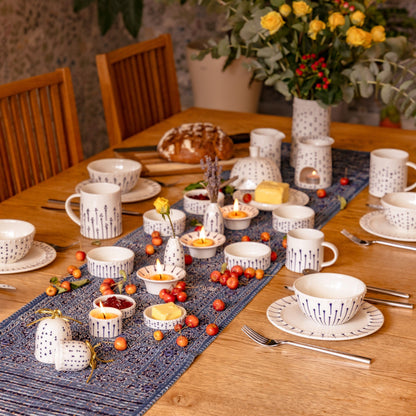 Handmade porcelain tableware with blue slip-trailed decoration styled on a breakfast table with bowls, mugs, plates and candles