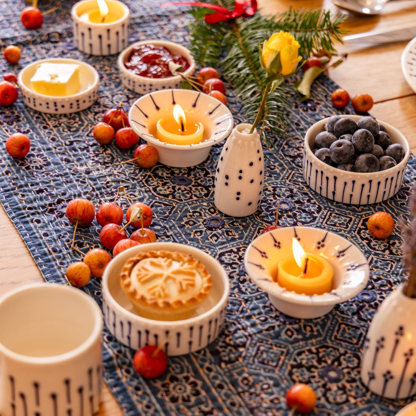 Handmade porcelain ramekins, candle holders, and mini vases with blue slip-trailed decoration styled on a table with berries and tealights