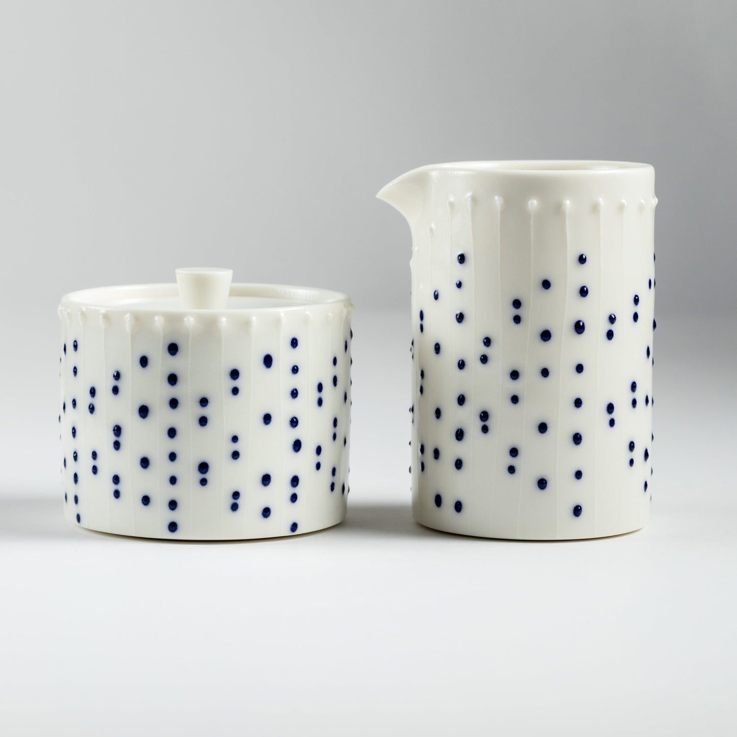 Handmade porcelain lidded jar and tall milk pourer with blue slip-trailed dot pattern