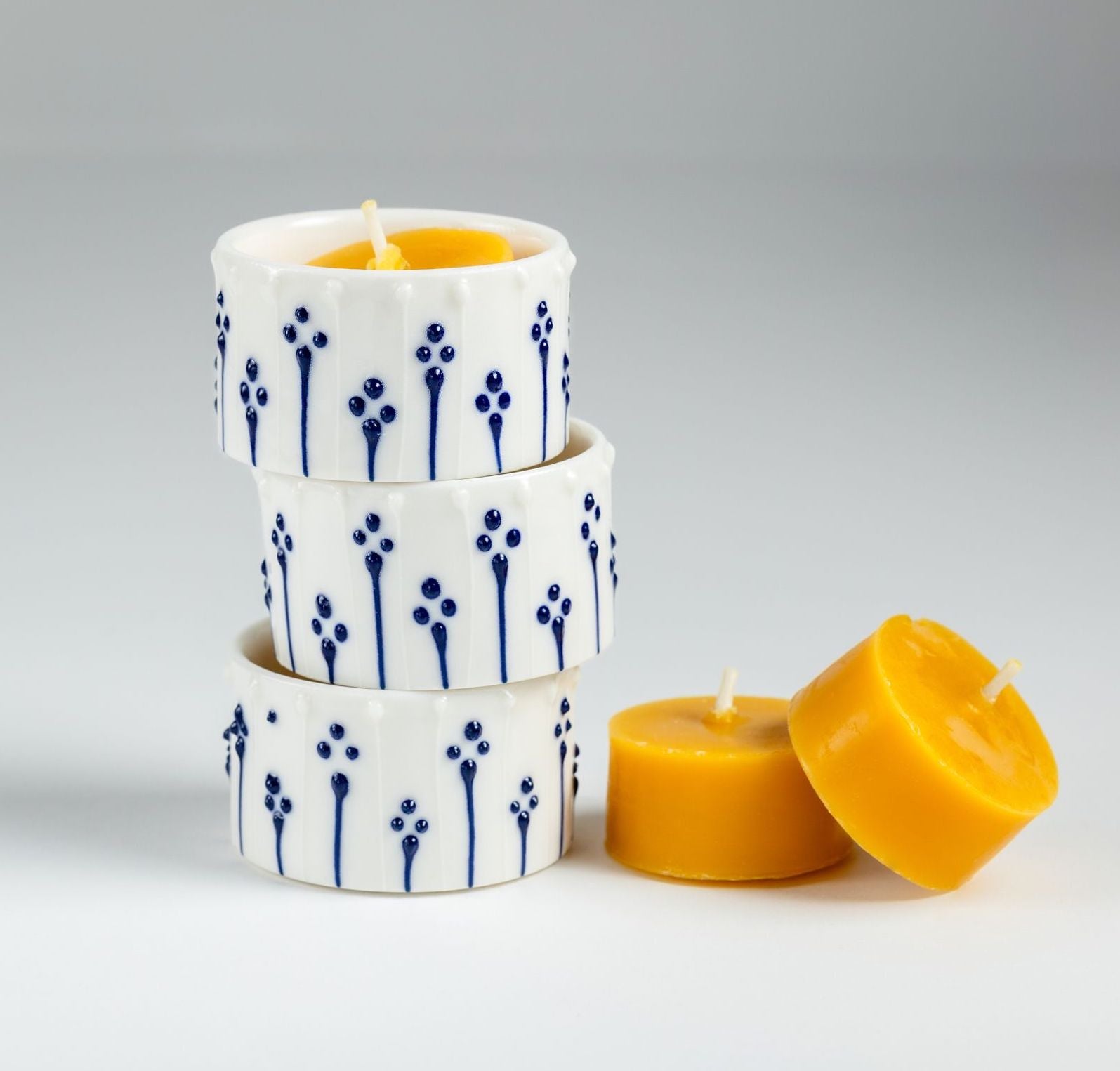 Natural beeswax tealight refills beside handmade porcelain tealight holders with blue slip-trailed decoration